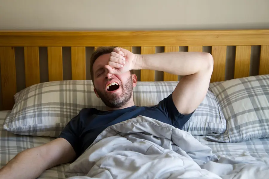 Homem acordando cansado, com a mão na testa, sinal comum de apneia do sono